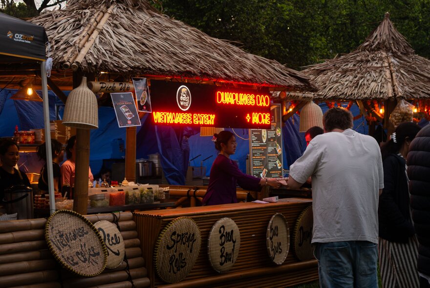 A food stall at dusk with the back of a man visible in the foreground. 