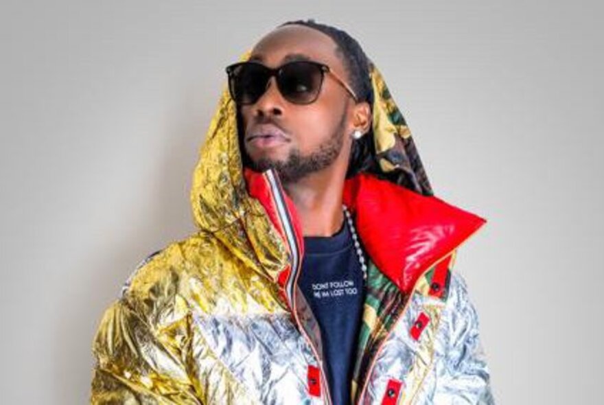 Musician Stylo G wearing sunglasses and a coloured puffy jacket with a hood. 