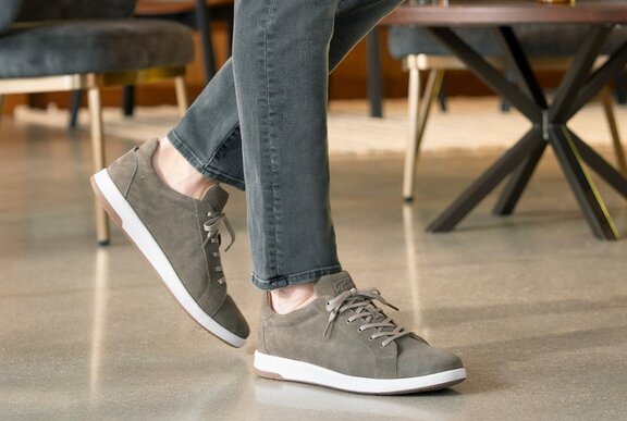 Person wearing grey sneakers and jeans stands on a polished floor in a modern room with grey chairs and a table.