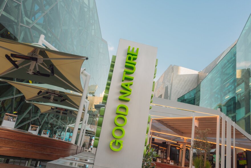 Exterior of Good Nature Hotel at Fed Square with green signage, and shade umbrellas.