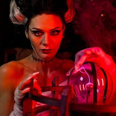 A woman dressed in a Halloween costume to look like Frankenstein's wife, with a crystal ball and smoke curling around her.