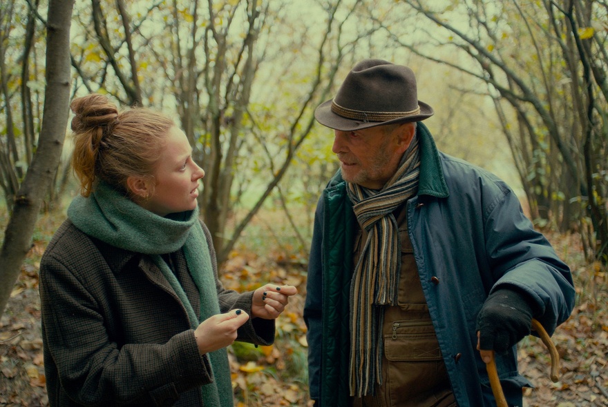A still image from a film showing a man and a woman talking seriously in the woods in winter.
