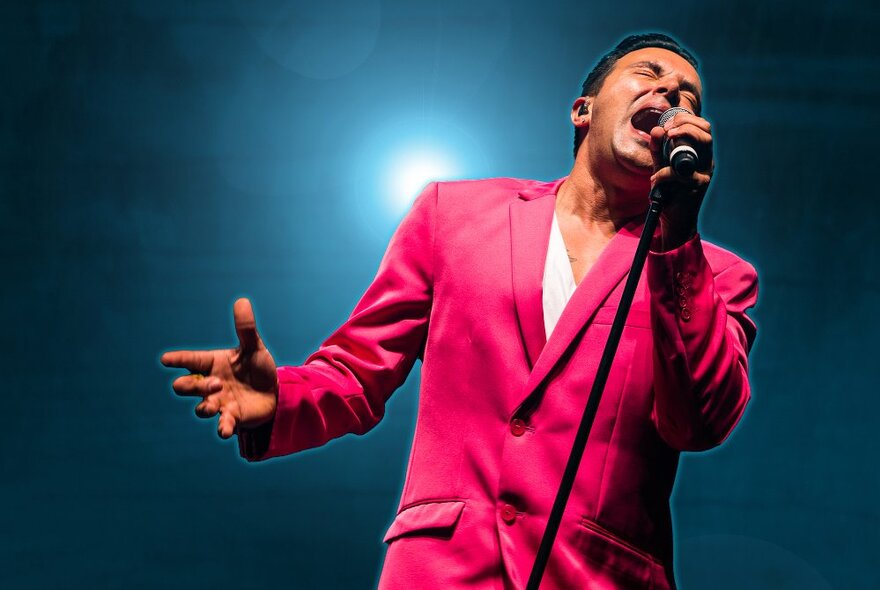 Singer Jason Singh wearing a pink jacket and singing into a microphone on a stage.