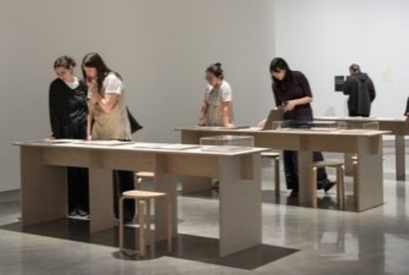 People gathered to look at display cases in a gallery setting.
