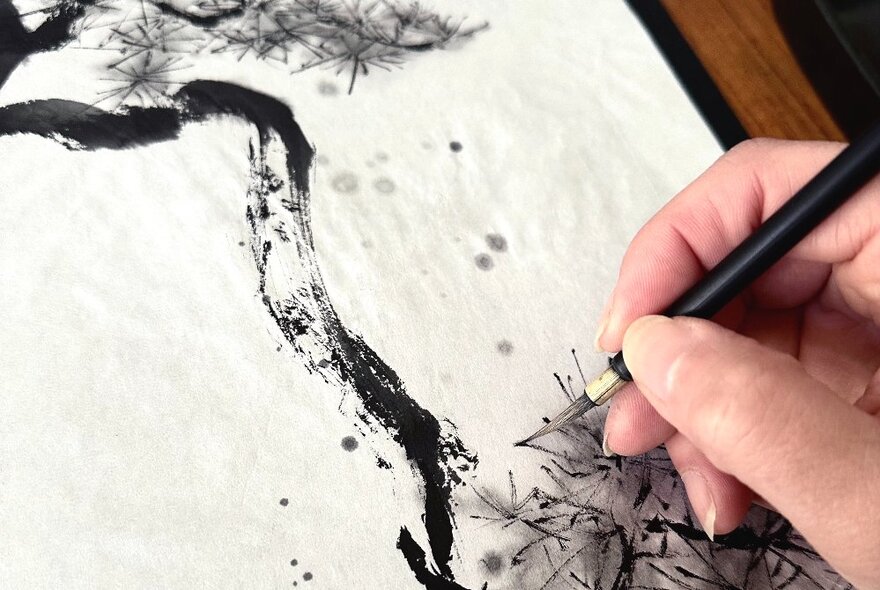 A hand holding a pen over paper and drawing in fine black ink strokes.