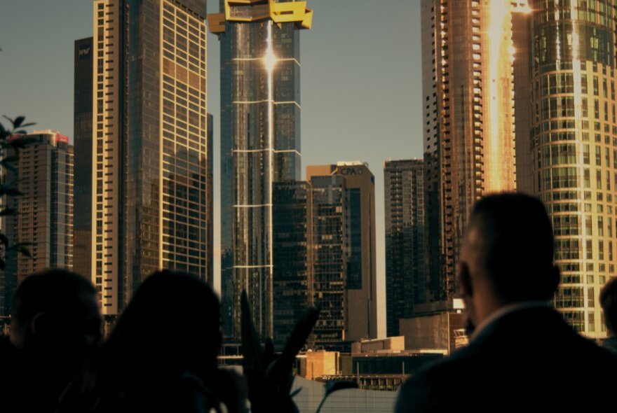 Melbourne city skyscrapers in the distance, as seen from a rooftop terrace at The Waterside Hotel, with a few people in silhouette in the foreground.