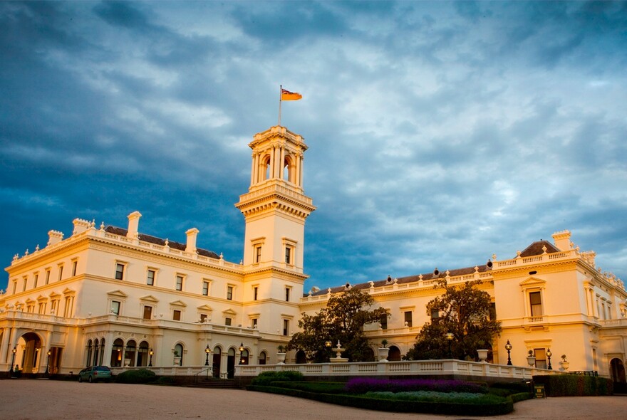 Three story, white, historic Government House building with tower and flag.