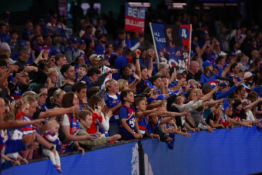 Western Bulldogs fans in the crowd with arms out. 
