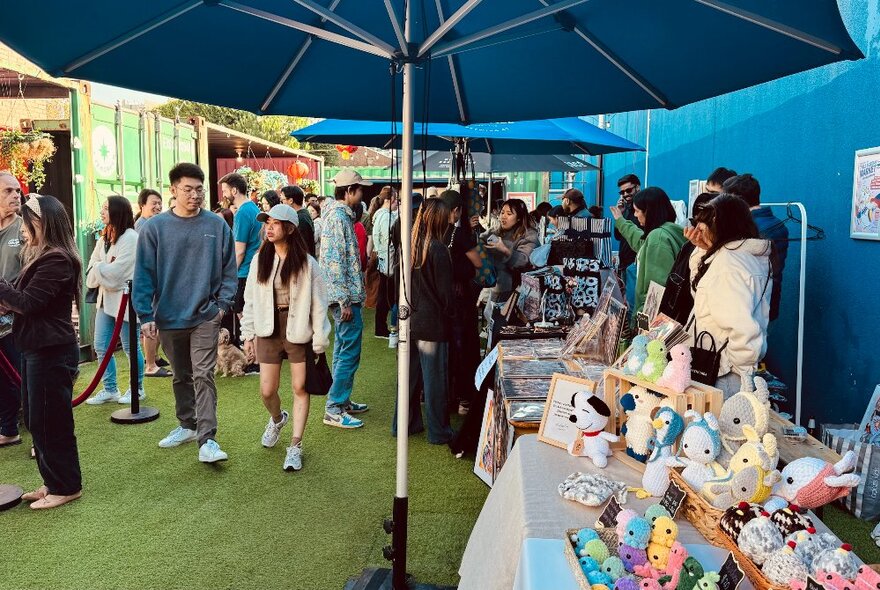 People walking past craft stalls at an outdoor market and looking at the items for sale.