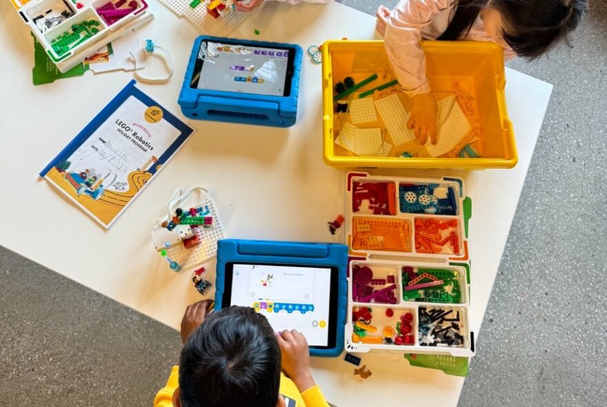 Looking down on a table with kids using tablets and coloured bricks. 