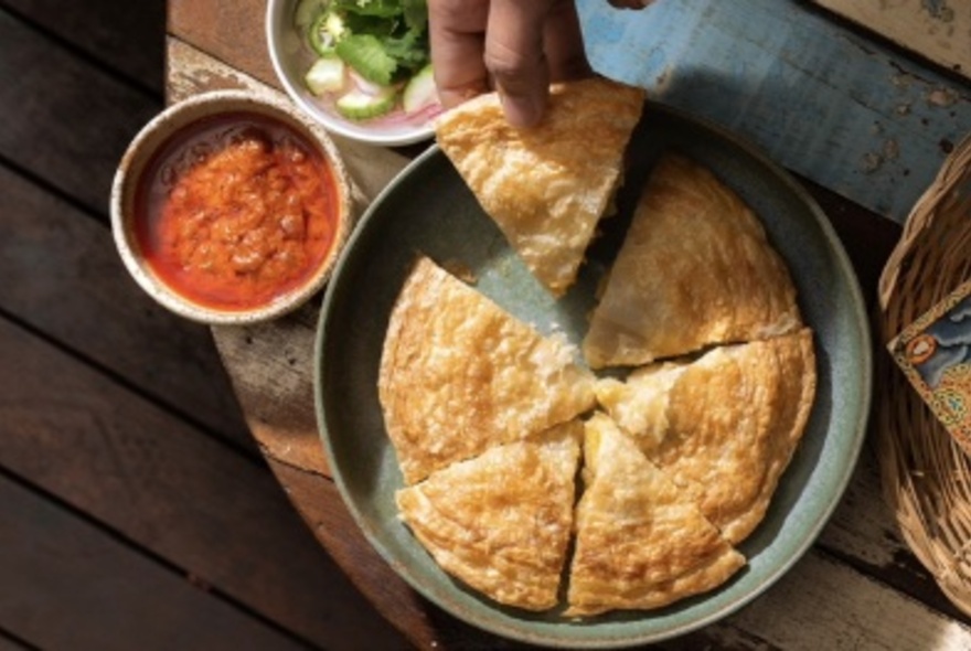 A hand taking a slice of pie from a round pie dish with condiments on the side.