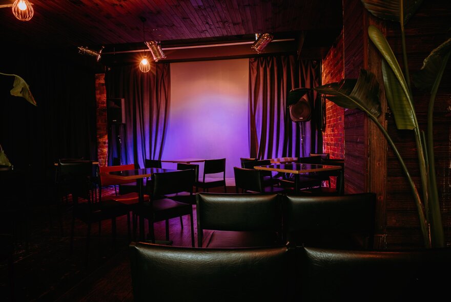 The purple-lit stage at the Motley Bauhaus, seen from behind empty audience chairs.