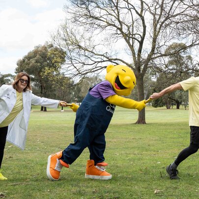 A community awareness and fundraising event in Princes Park, Carlton, with a mascot holding hands with a runner and a person in a white scientist's coat.