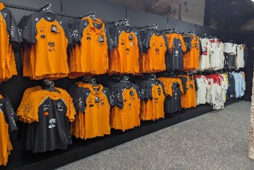 A wall of a shop lined with yellow and black branded F1 polo shirts.