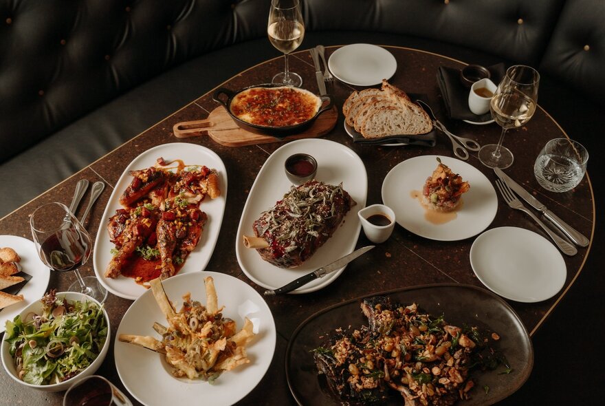 Looking down at a table in a restaurant, that is filled with plates of food, and glasses of wine.