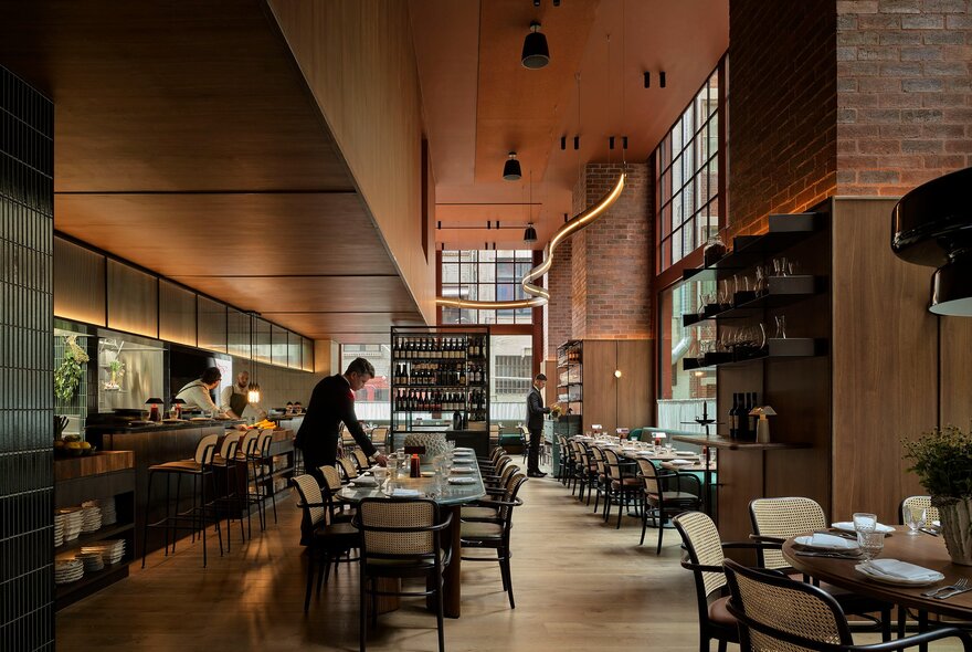 The long interior of a restaurant with a bar to the left and a long table set for service down the middle.