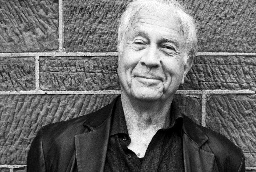 Author and historian Henry Reynolds, a man in his senior years, smiling, with white hair, posed against a brick wall; a black and white image.