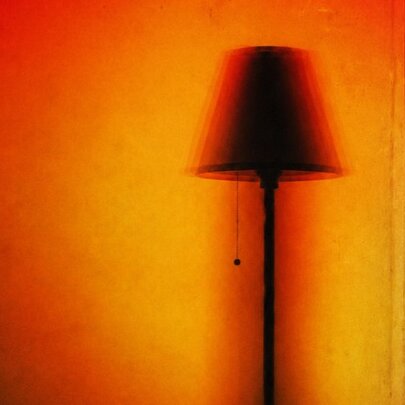 The silhouette or shadow of a standing lamp against a golden orange background.