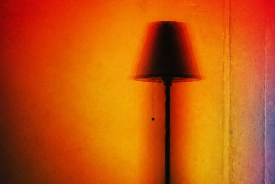 The silhouette or shadow of a standing lamp against a golden orange background.