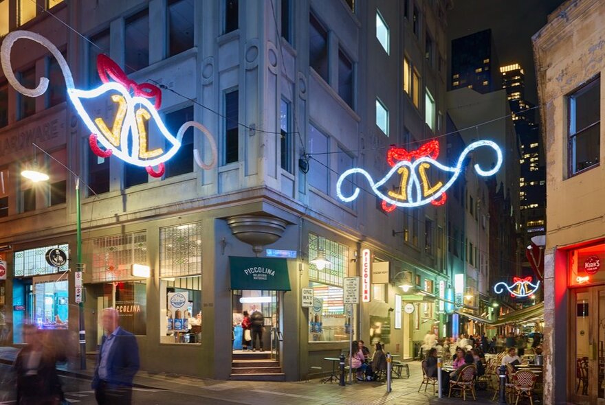 Light up Christmas bell decorations over a laneway full of people. 