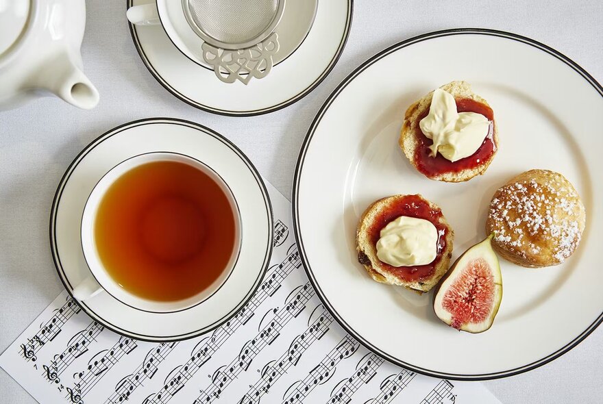 Looking down at a cup of tea and a plate of scones with jam and cream as part of a High Tea menu.