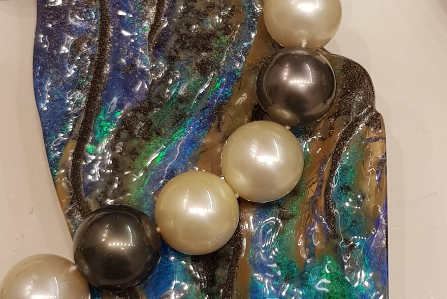Black and white pearl necklace draped over coloured stone.