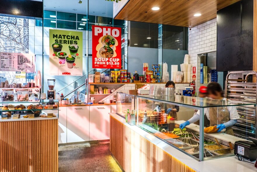 The interior of the Bammi Vietnamese takeaway shop in Melbourne with a woman behind a counter making banh mi and posters on the glass walls. 