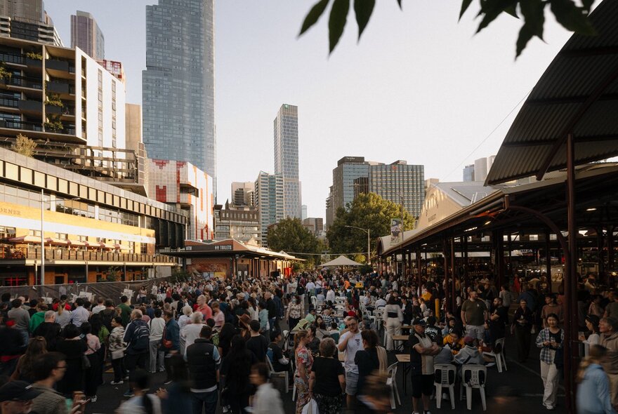 Large crowd standing outside the Queen Victoria Market sheds at dusk.