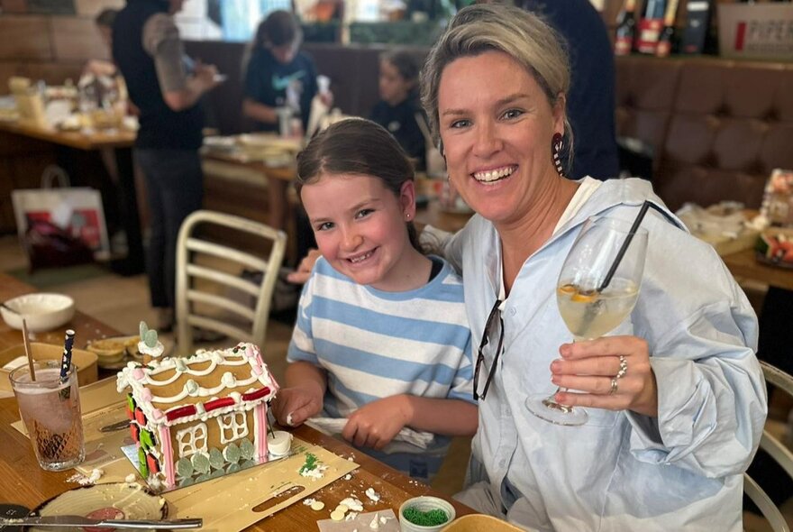 A woman and young girl at a gingerbread house decorating workshop, the woman holding a drink with a straw, 
