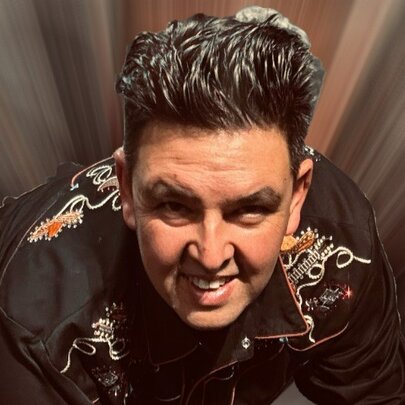 A man with big hair crouching down and looking straight ahead with dark coloured beams all around him. 