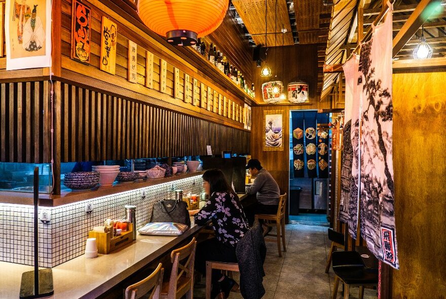 Two people are sitting in a small ramen restaurant