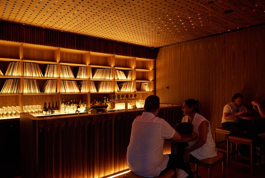 Two friends are in a dimly-lit bar surrounded by vinyl records.