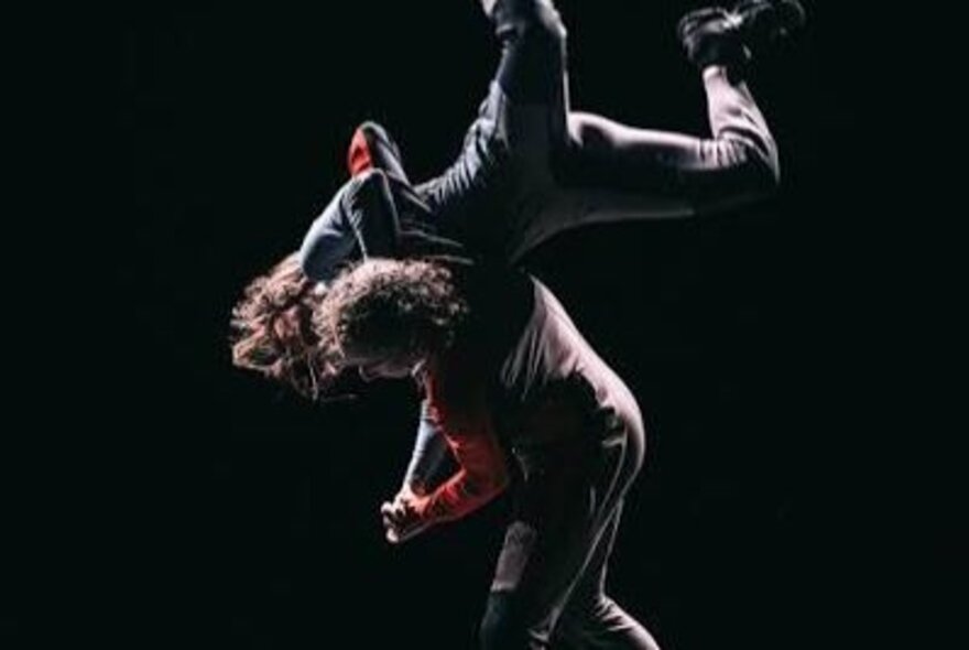 Dancers performing in spotlit darkness.