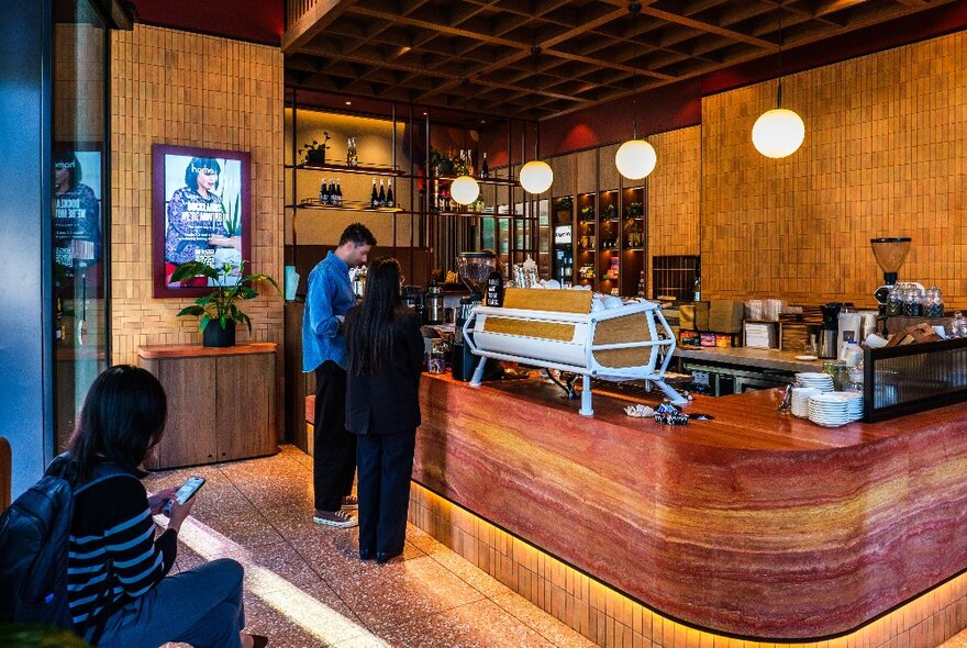 Two people standing at the wooden counter of a cafe with a coffee machine on top. 