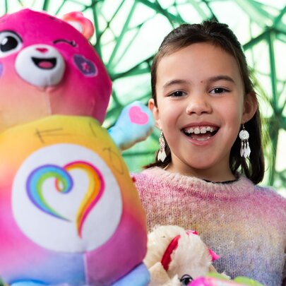A smiling child holding a large pink soft toy.