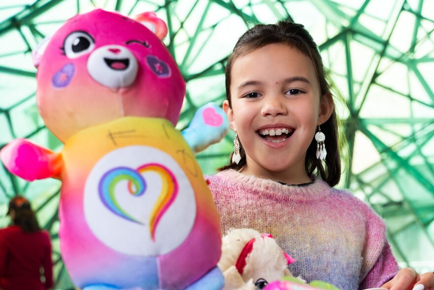 A smiling child holding a large pink soft toy.
