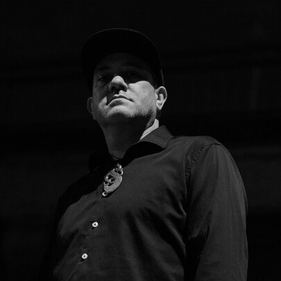 A black and white photograph of a man with his face half in shadow, blackness all around him.