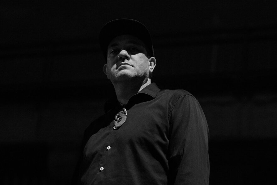 A black and white photograph of a man with his face half in shadow, blackness all around him.