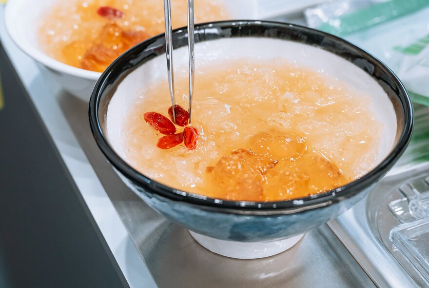 A dessert bowl with tapioca pears and small red berries being added with tweezers. 