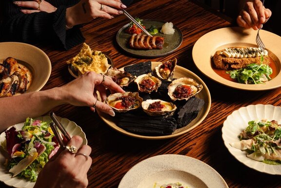 A table laden with a banquet of dishes including fresh oysters, wagyu beef, gyoza and salad.