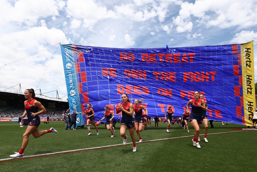 Melbourne Demons AFLW players running through the banner at the start of the game.