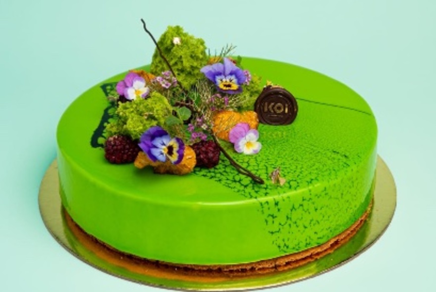 A round cake, iced in verdant green, with floral and chocolate decorations on top.