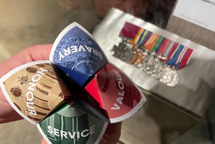 Hands holding a paper folding game in front of a row of medals.