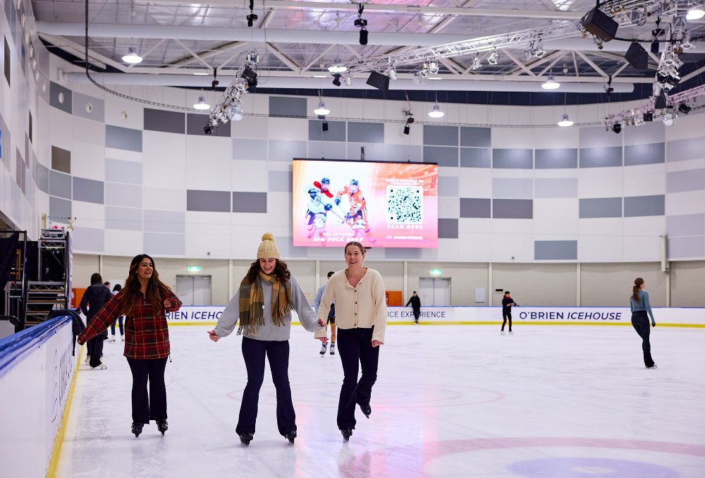 Three friends skating on an indoor ice rink.