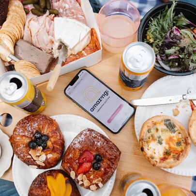 Picnic spread of dishes, boxed food and drinks on a blue gingham tablecloth.