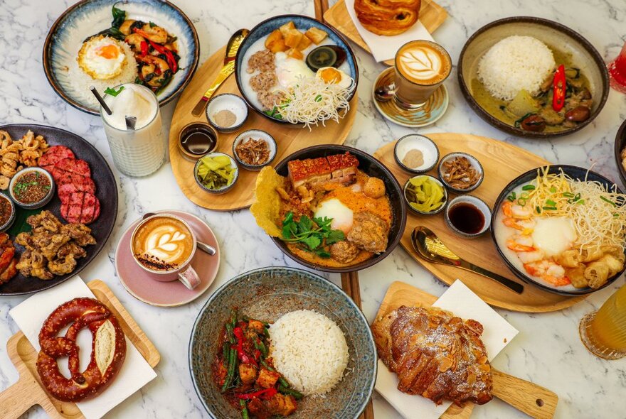 Dining table laden with Thai dishes of food and condiments including noodle and rice dishes.