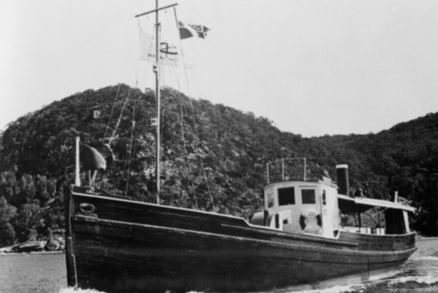 A black and white photo of a wooden boat in WWII just off a coastline. 