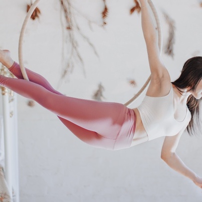 Person balanced in an aerial hoop, legs extended behind her, against a white wall.