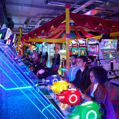 Three people playing a water gun game in a neon-lit arcade.