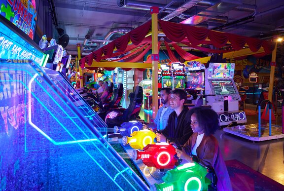 Three people playing a water gun game in a neon-lit arcade.